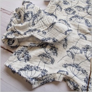 Muślinowy kombinezon niemowlęca. Przewiewny dziewczęcy rampers. Kombinezon na lato z czapeczką dla niemowlaka. Biały rampers muślinowy w kwiaty dla małej dziewczynki.