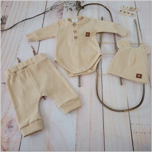 Prążkowany zestaw dla niemowlaka. Komplet całoroczny w  kolorze beżowym. Prążkowane spodnie w komplecie z body i czapką dla niemowlaka.