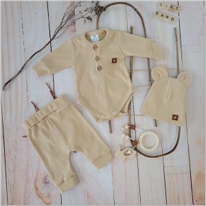 Prążkowany zestaw dla niemowlaka. Komplet całoroczny w  kolorze beżowym. Prążkowane spodnie w komplecie z body i czapką dla niemowlaka.