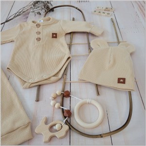 Prążkowany zestaw dla niemowlaka. Komplet całoroczny w  kolorze beżowym. Prążkowane spodnie w komplecie z body i czapką dla niemowlaka.