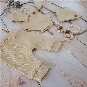 Prążkowany zestaw dla niemowlaka. Komplet całoroczny w  kolorze beżowym. Prążkowane spodnie w komplecie z body i czapką dla niemowlaka.