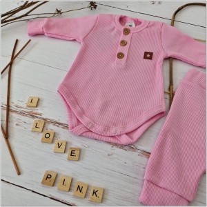 Prążkowany zestaw dla niemowlaka. Komplet całoroczny w  kolorze różowym. Prążkowane spodnie w komplecie z body i czapką dla niemowlaka.